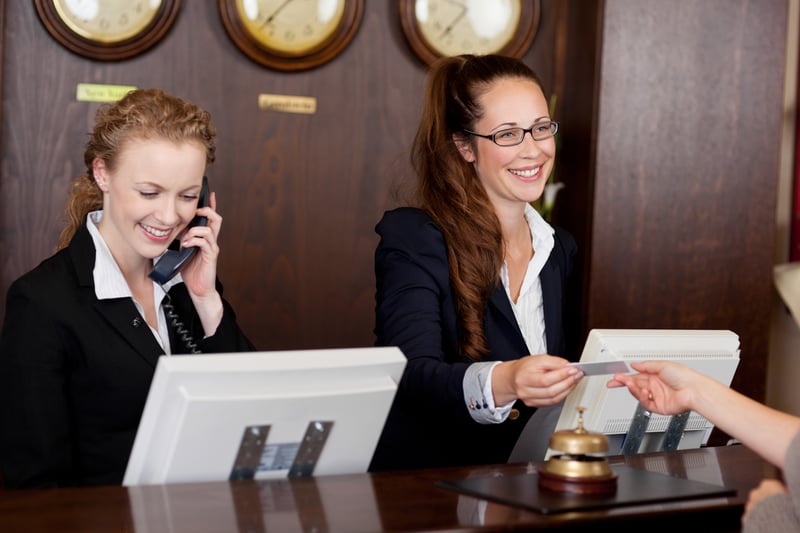 Two beautiful young stylish receptionists at a reception desk, one talking on the telephone and the other handing a card to a customer Two beautiful young stylish receptionists at a reception desk, one talking on the telephone and the other handing a card to a customer